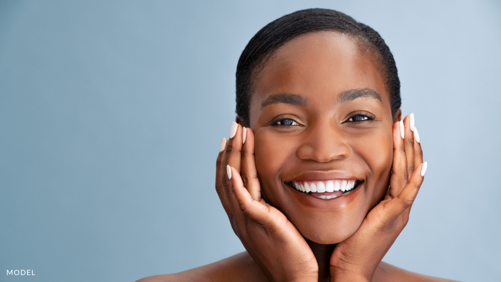 A younger woman touching her face and smiling (model)