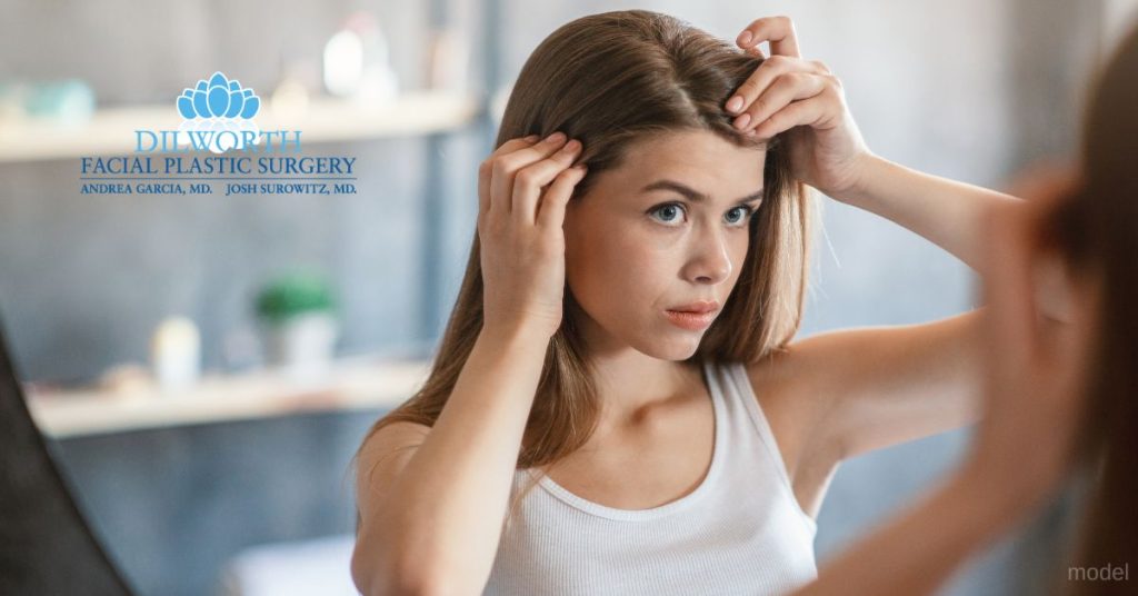 A woman combing their hair in front of a mirror. (Model)