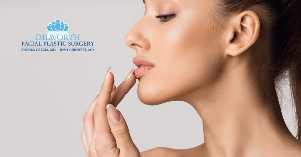 A woman facing her side, touching her lips with her hand. (Model)